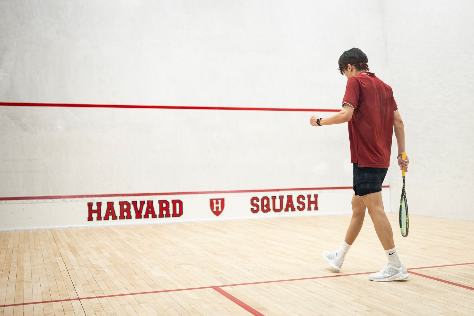 Jacob Lin on court at the Harvard squash facility, racket in hand, walking toward the front wall.
